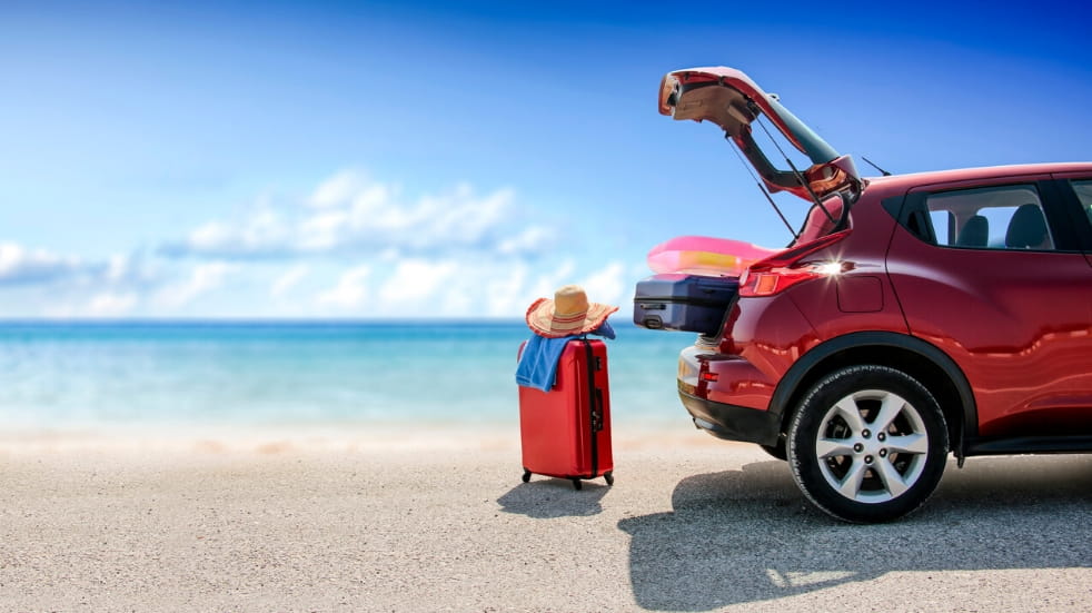 Car parked on beach with boot open and suitcases
